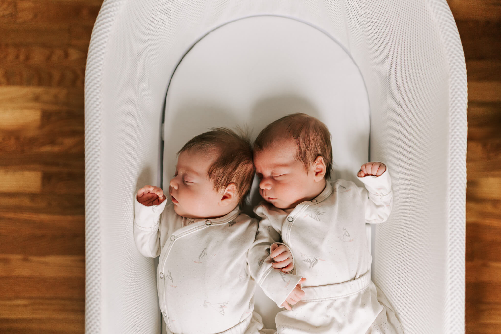 newborn twins sleeping together in a snoo