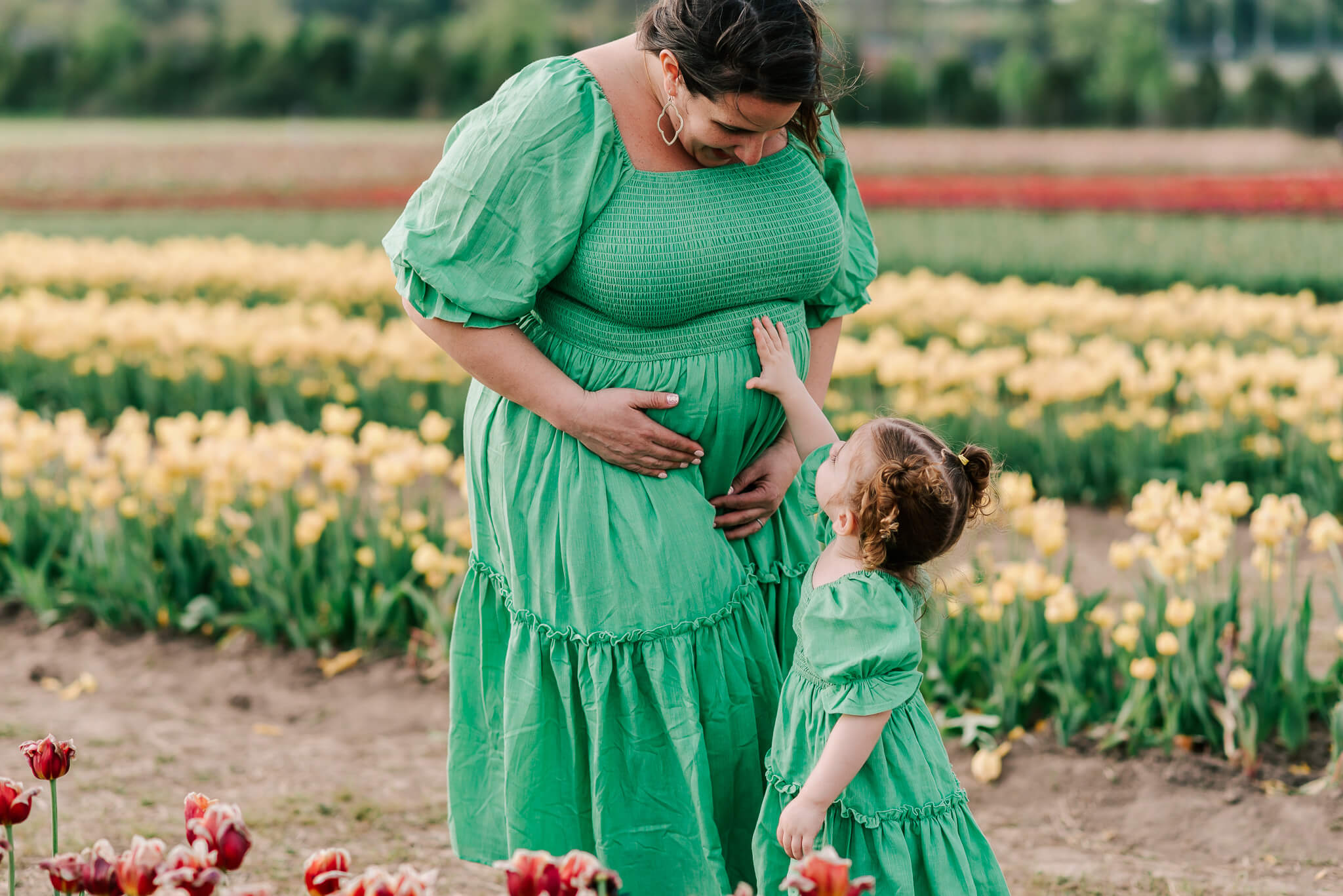 Daughter patting her mother's pregnant belly in a tulip field, touch therapeutic massage