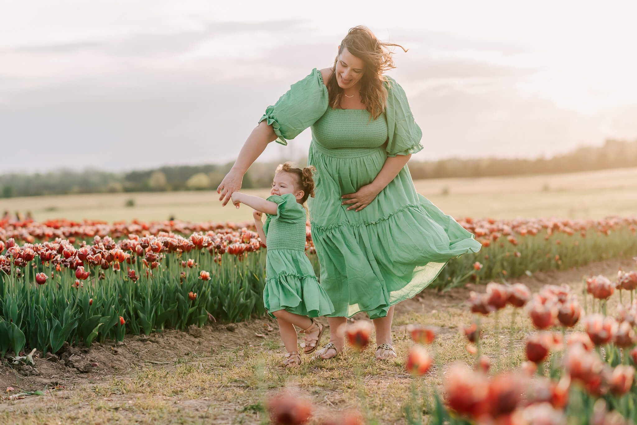 A mama twirling her daughter in a tulip field at sunset in Burnside Farms, touch therapeutic massage