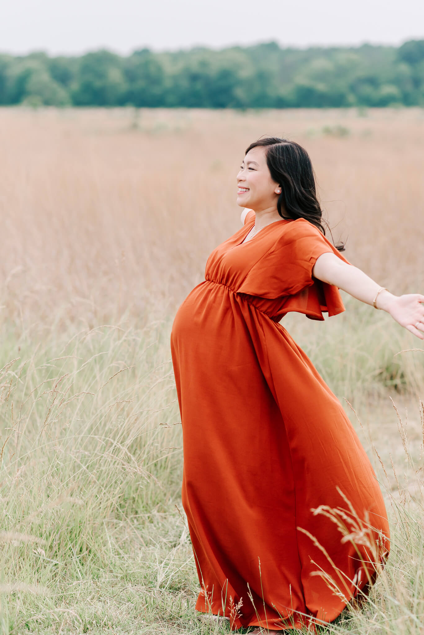 asian woman in a rust maternity gown joyfully stretching her arms out, Sage Midwifery