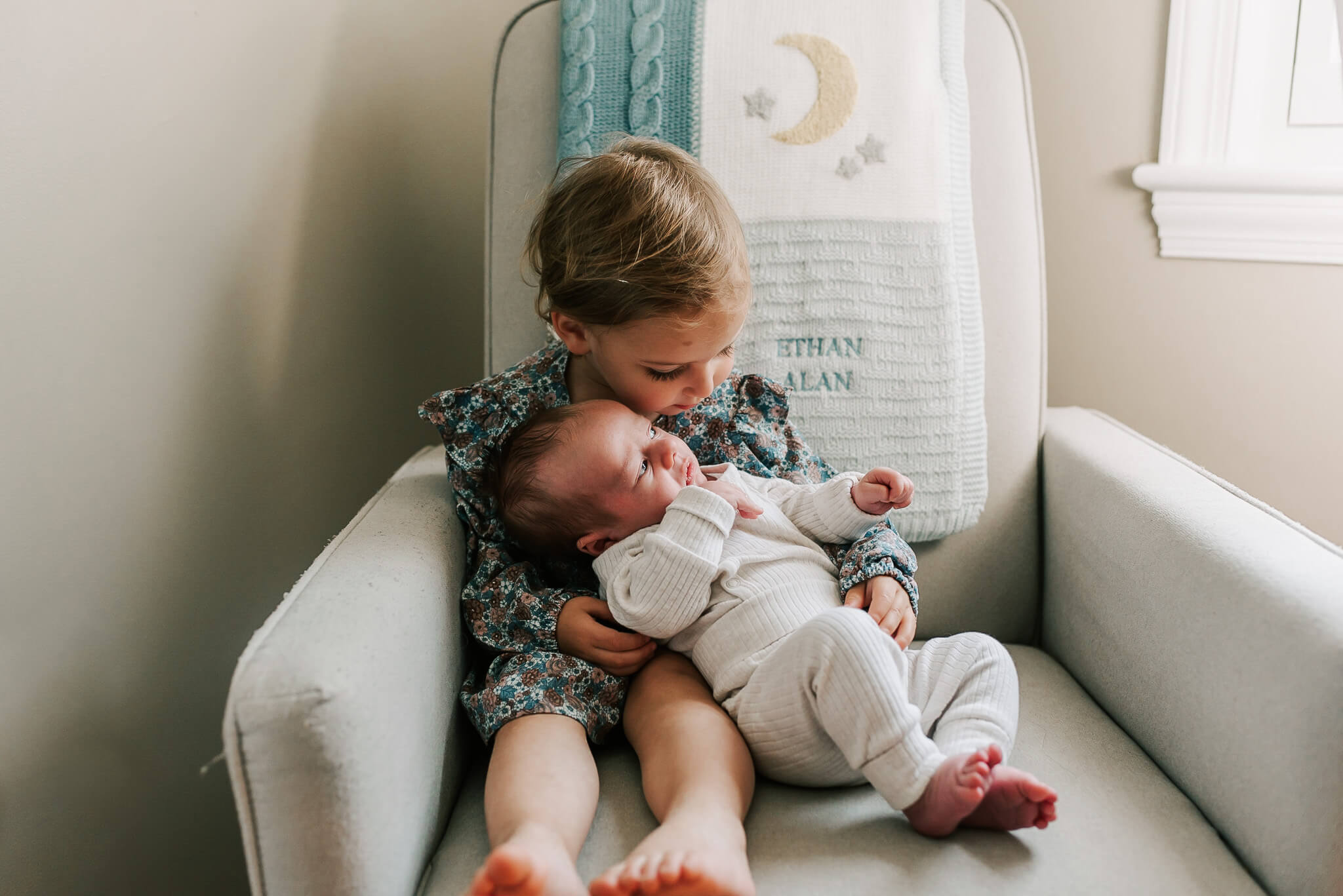 A big sister holds her newborn baby brother in a recliner momease