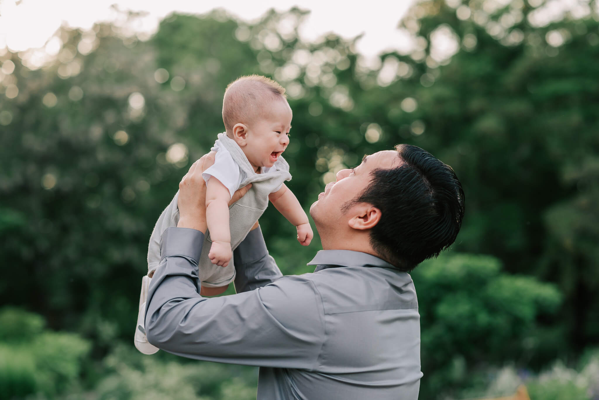 A dad lifts his baby son up into the air and earns a sweet smile from the baby, NOVA birth partners