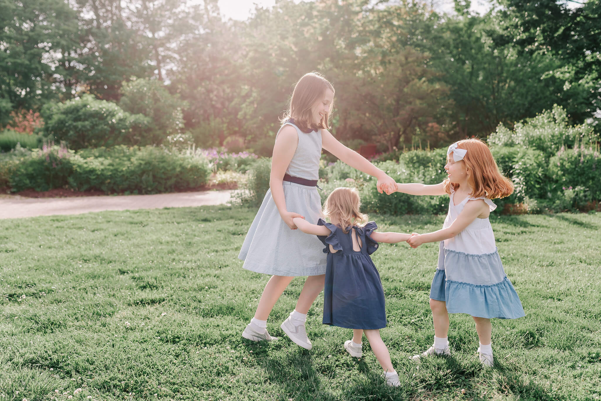 Three sisters in blue dresses hold hands and play in circles in a flower garden Scramble Alexandria