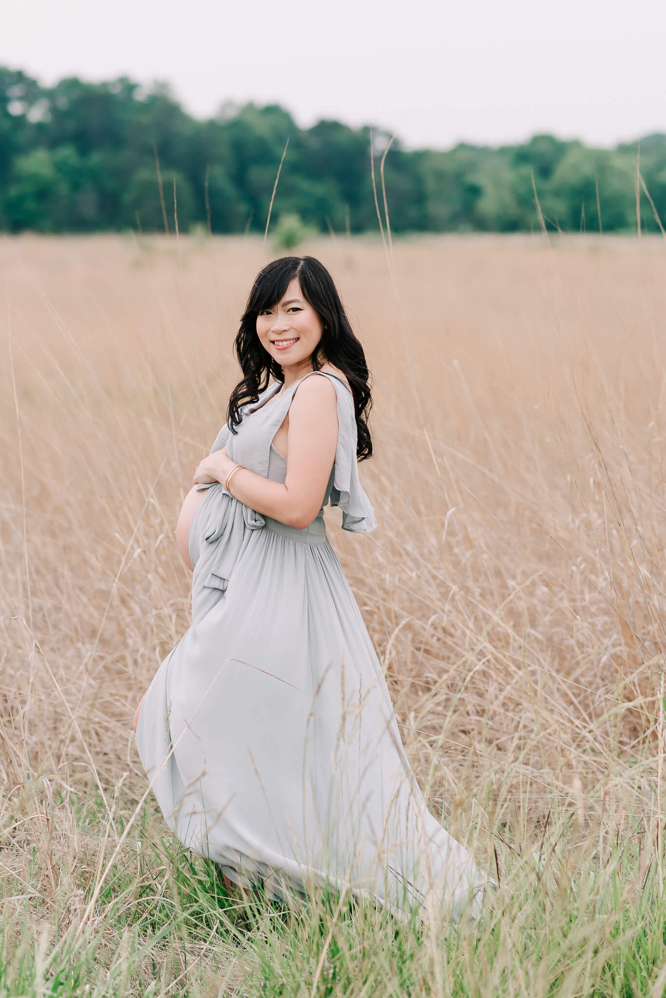 A mother to be stands in a field of tall grass while holding her bump prenatal yoga northern virginia