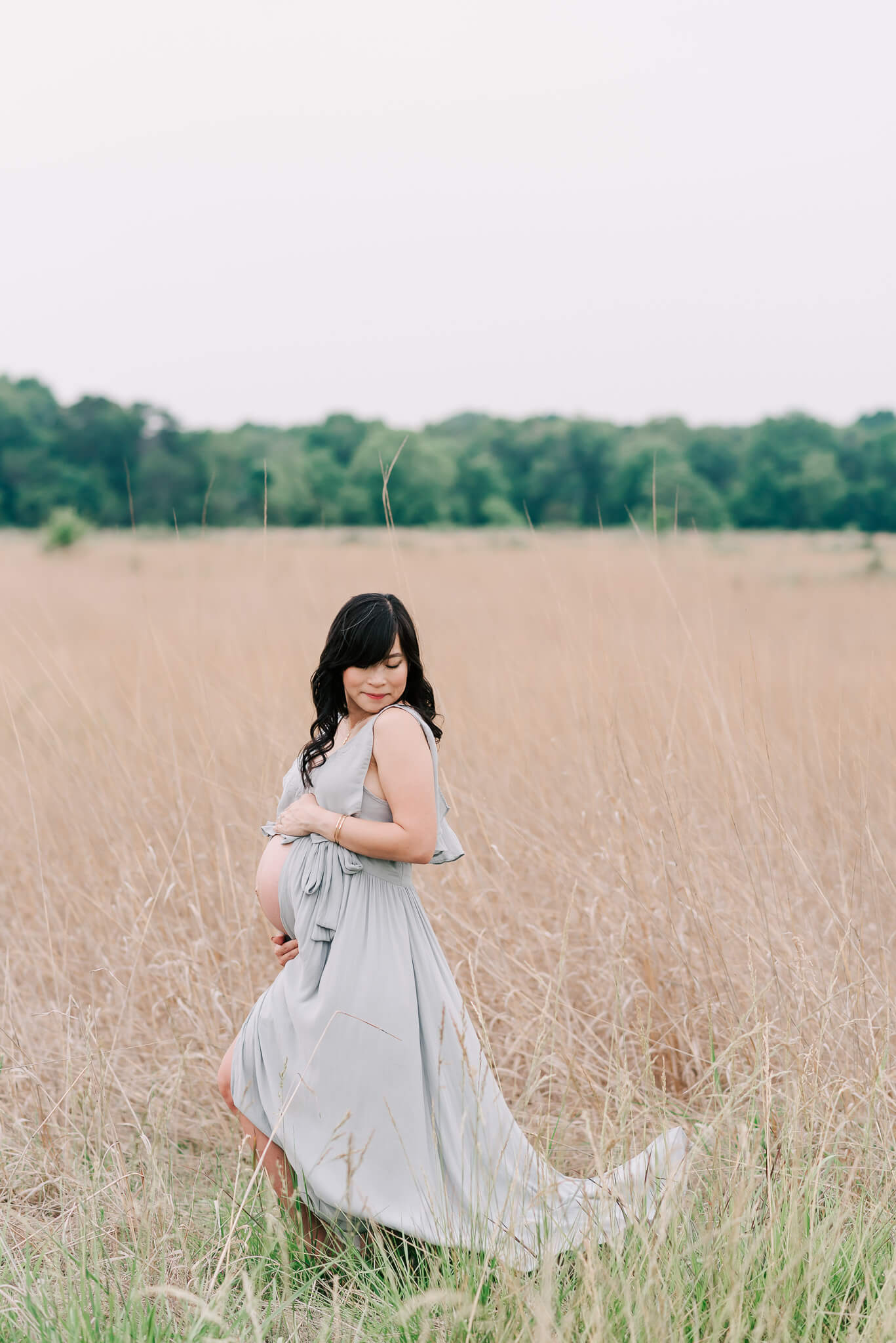 A mom to be walks through a field of tall grass in a long green maternity gown prenatal yoga northern virginia
