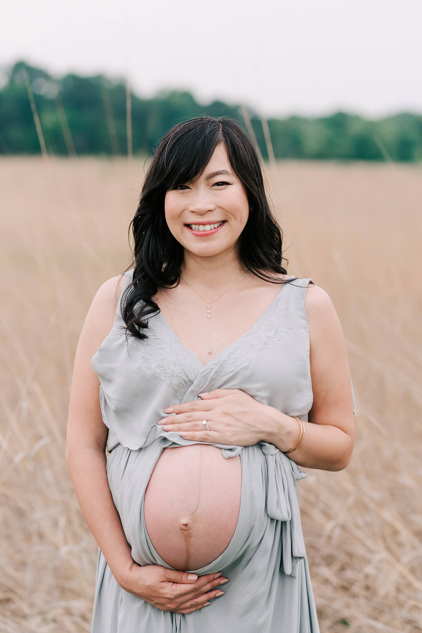 A mother to be stands in a field of golden grass while holding her exposed bump prenatal yoga northern virginia