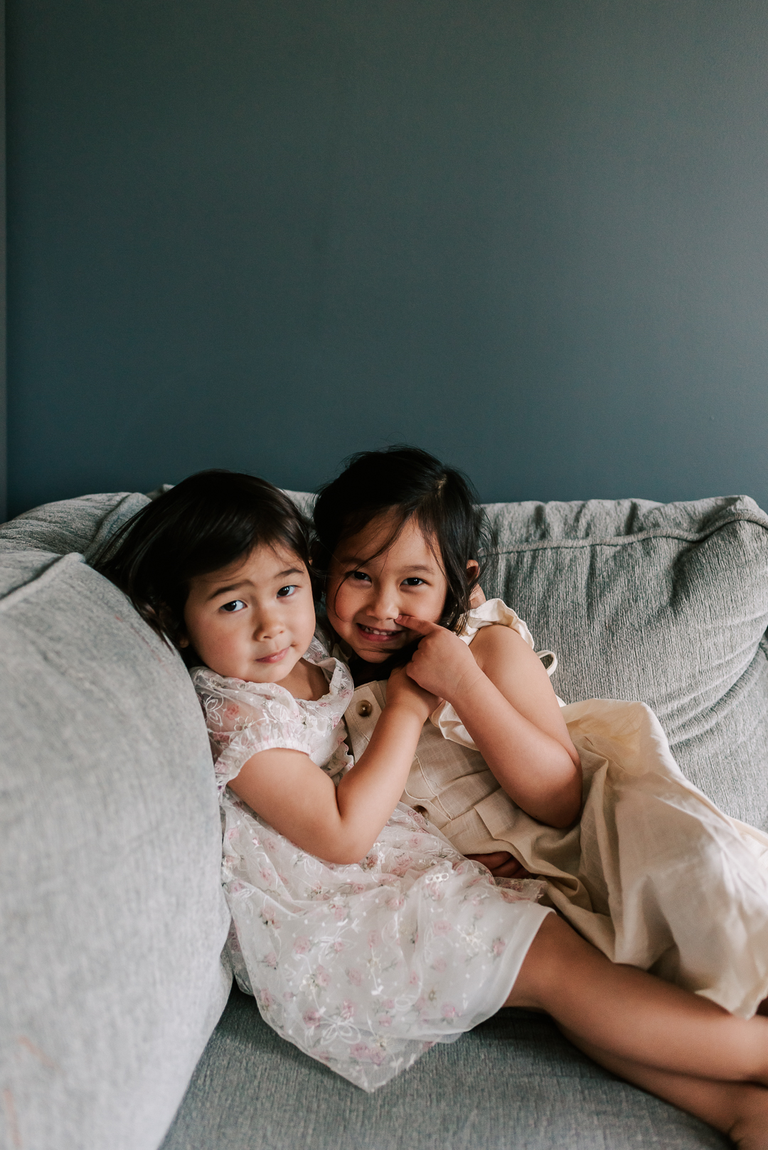 Two toddler sisters hug and smile on a couch in 529 kids consign dresses