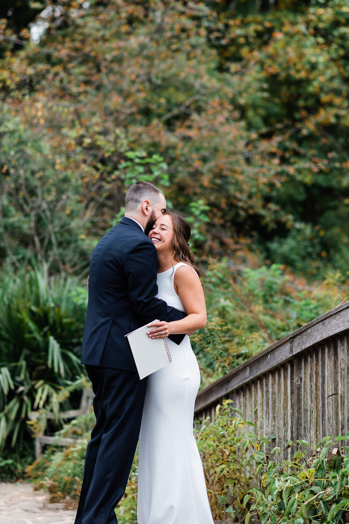 Newlyweds embrace while standing on a wooden bridge in meadowlark botanical gardens after their wedding ceremony