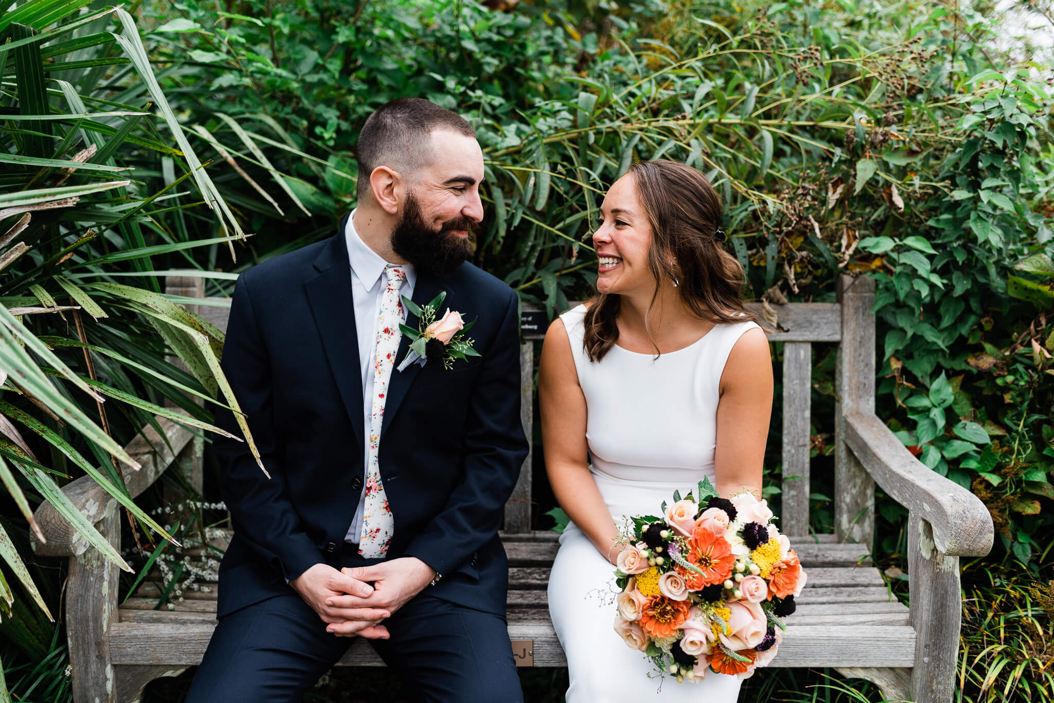 Newlyweds sit on a wooden bench smiling at each other at their meadowlark botanical gardens wedding