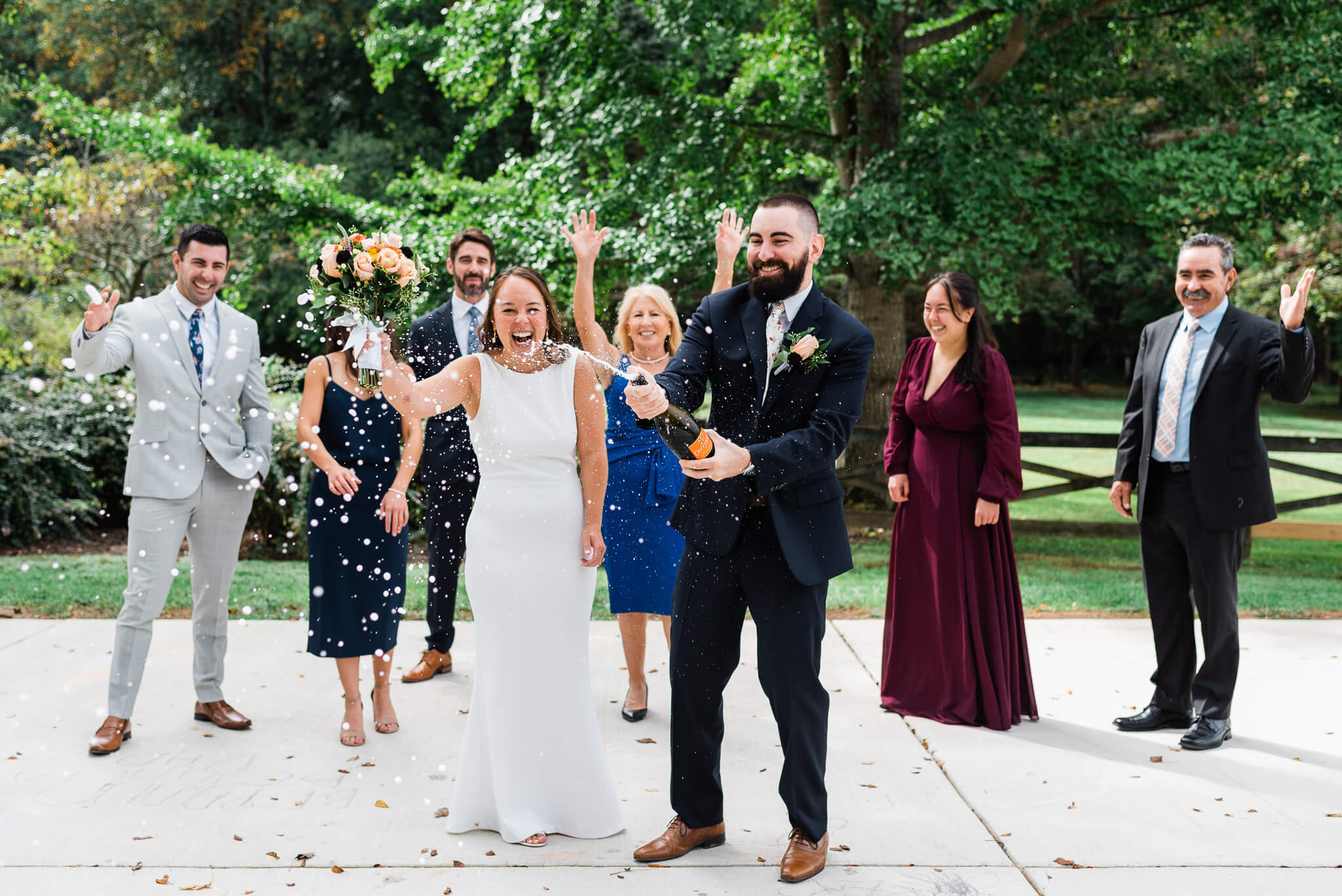 Newlyweds pop Champagne while standing in a patio at meadowlark botanical gardens with their wedding party cheering behind them