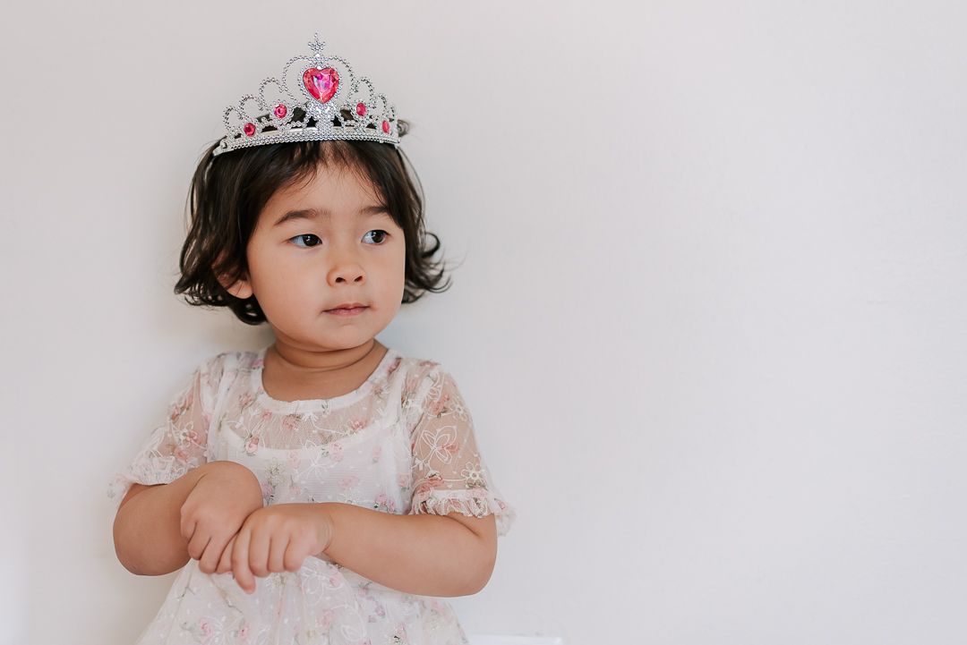 A young girl stands in a studio in a white and pink dress and pink and diamond tiara after visiting pump it up alexandria