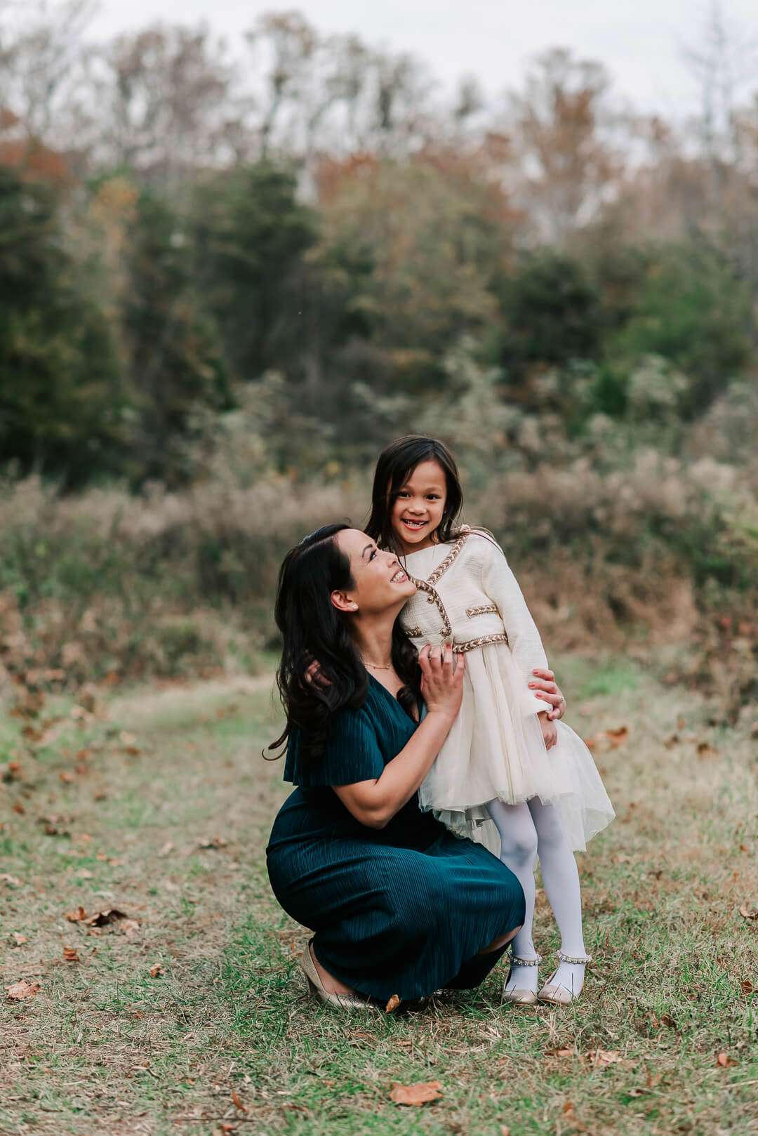 A happy mother sits squats to hug her young daughter in a park after meeting an annandale obgyn