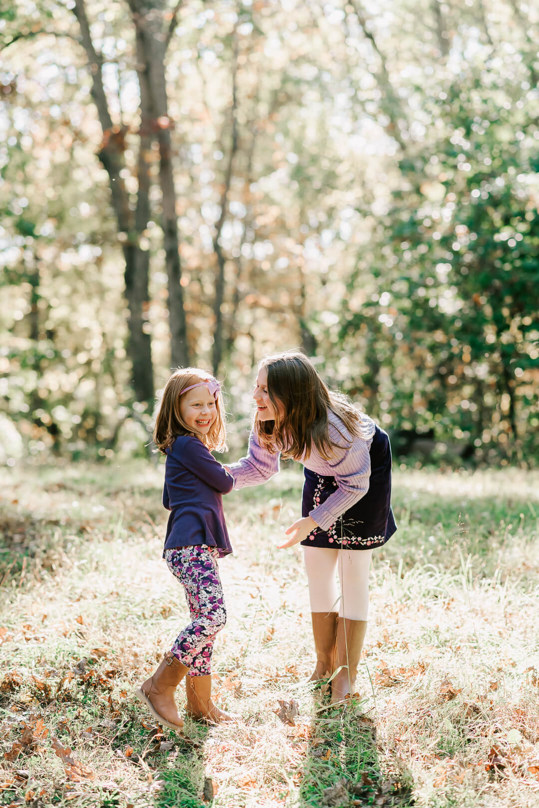 A young girl plays with her little sister in a forest wearing purple