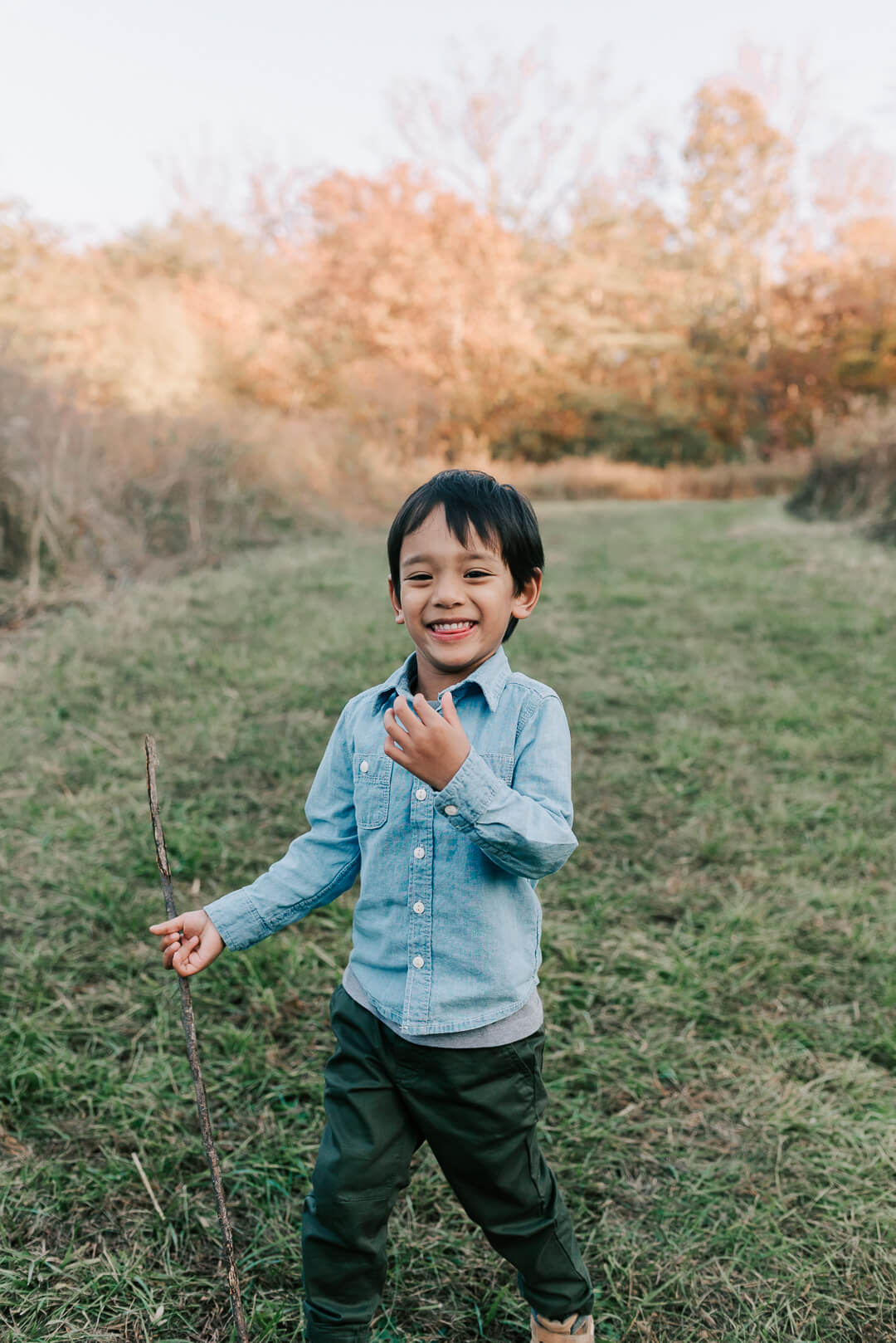 A young boy plays with a stick and laughs while walking through a grassy trail after visiting a falls church pediatric dentistry
