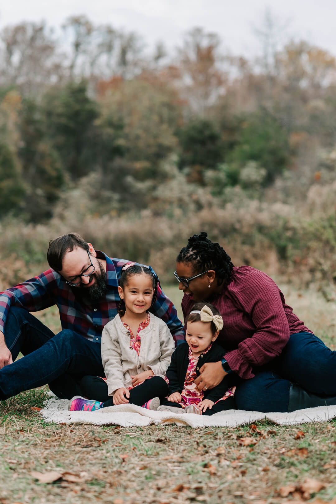 A mom and dad sit on a picnic blanket playing with their two toddler daughters after finding a mclean pediatrician
