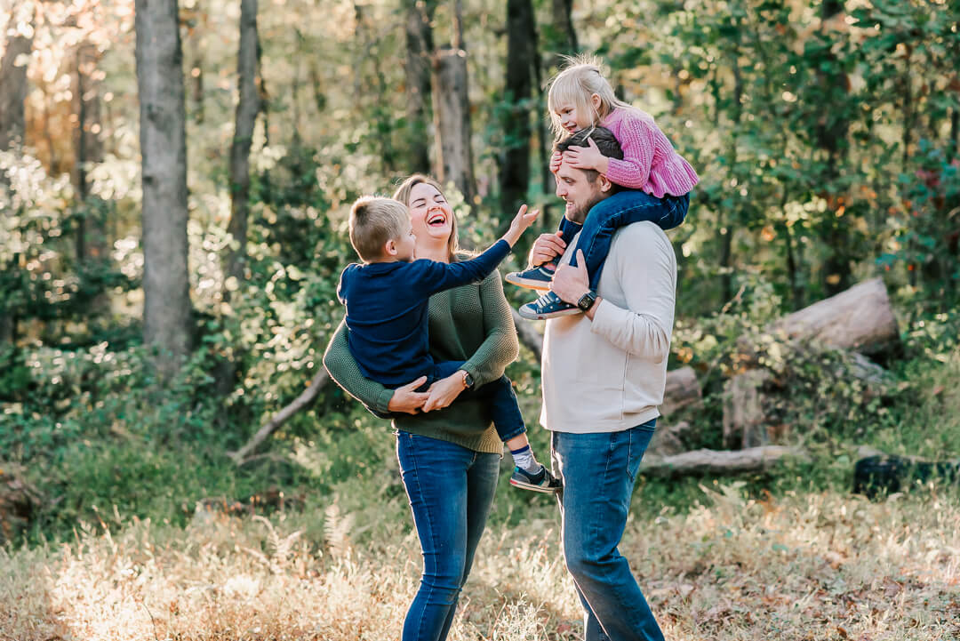 A mom and dad carry their toddler son and daughter on their shoulders and hip while standing in a forest after meeting with tysons pediatric dentistry