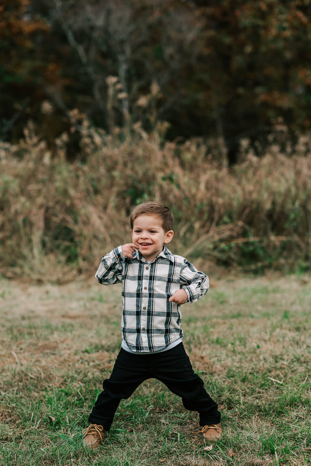 A young toddler boy in a plaid shirt plays in a clemyjontri park field