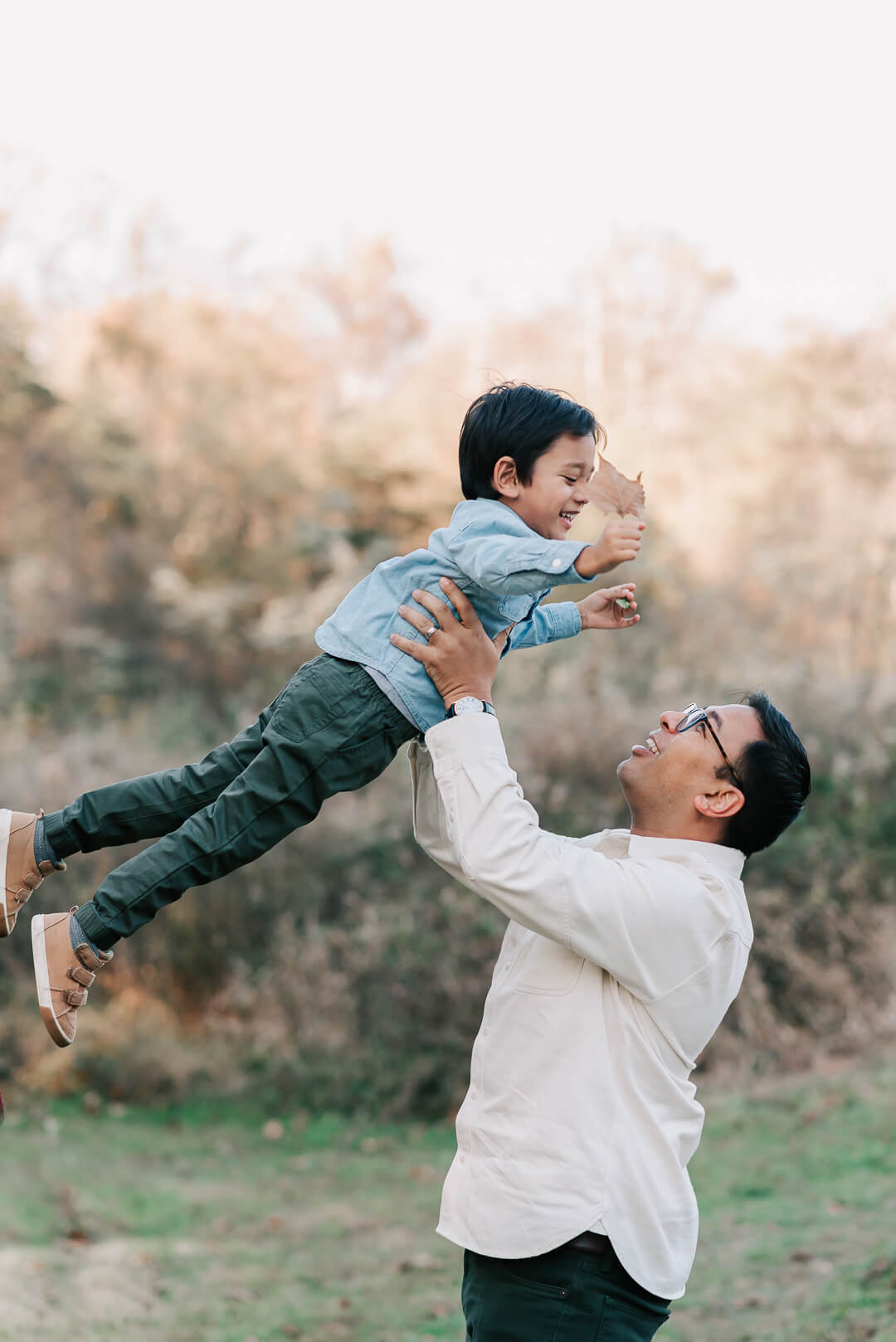 A happy father lifts and tosses his toddler son in the air in a park at sunset