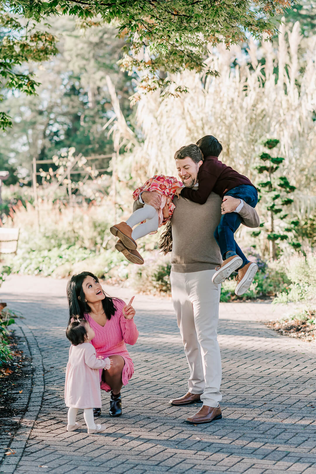 A father lifts his two toddler children over his shoulders while walking in a garden trail with mom and youngest watching during things to do in tysons corner