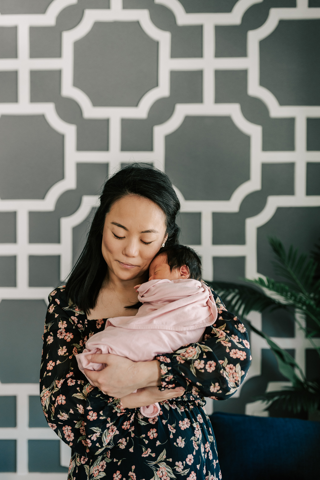 A happy new mother cradles her sleeping newborn baby against her cheek while standing inside after visiting northern virginia lactation consultants