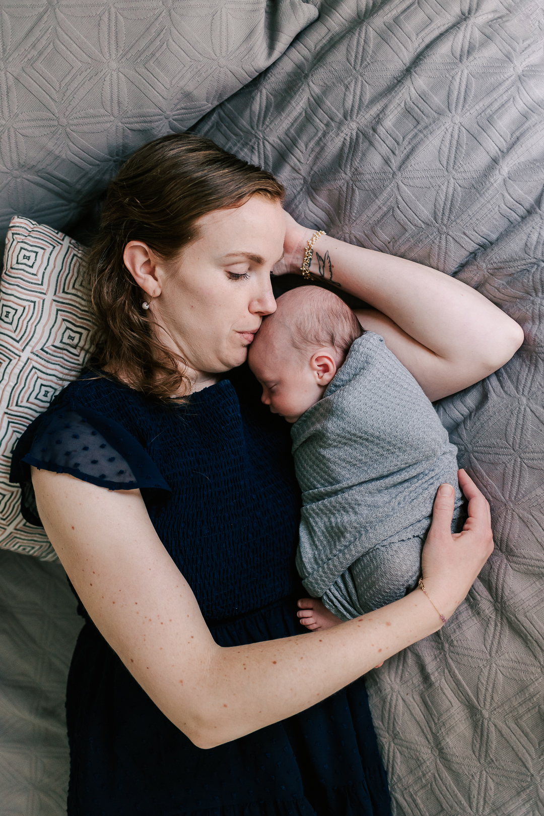A new mother lays on a bed snuggling her sleeping newborn baby in a blue dress before some pelvic floor therapy northern virginia