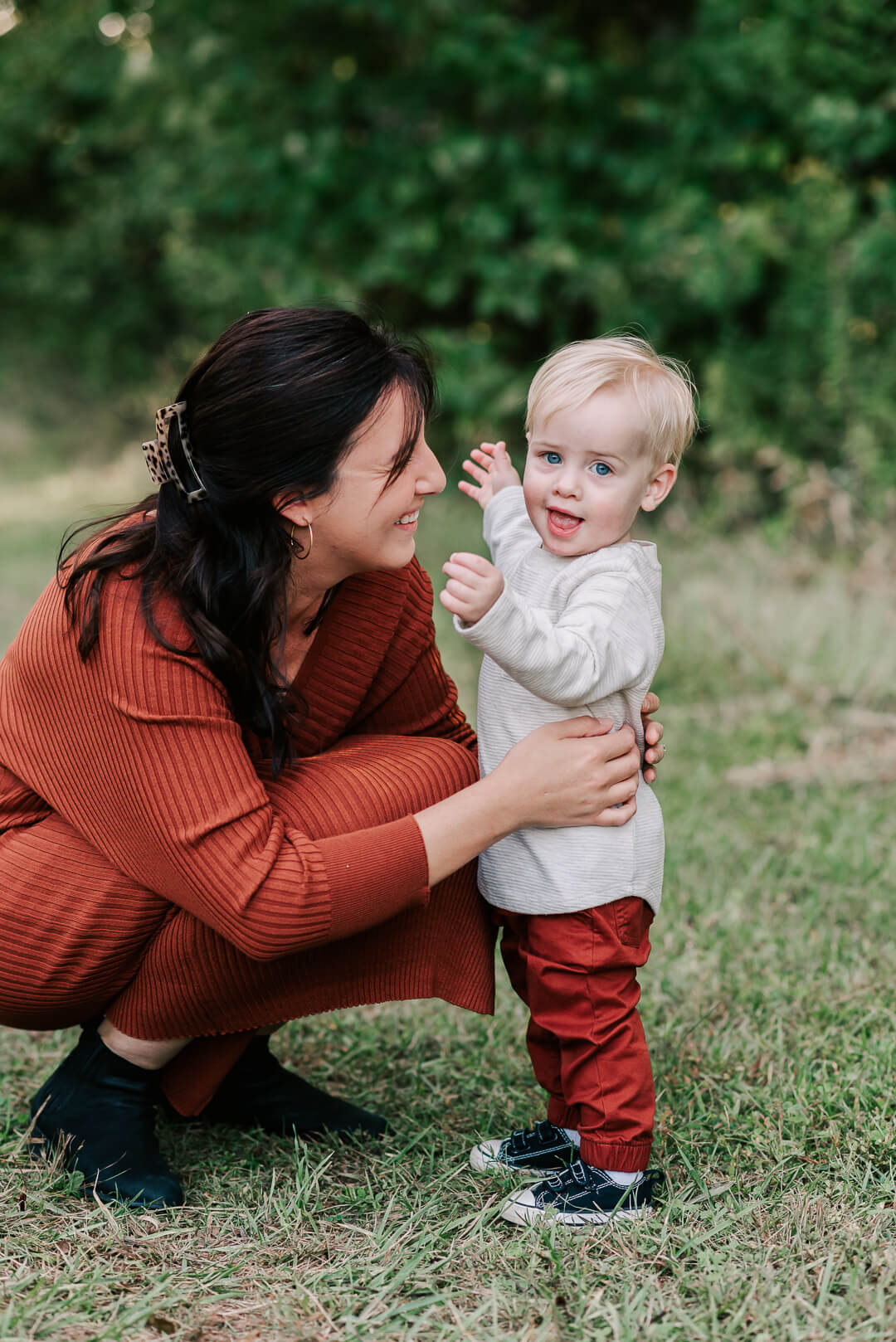A happy mother plays with her talkative toddler son in a park field of grass while wearing a red dress before visiting a childrens museum northern virginia