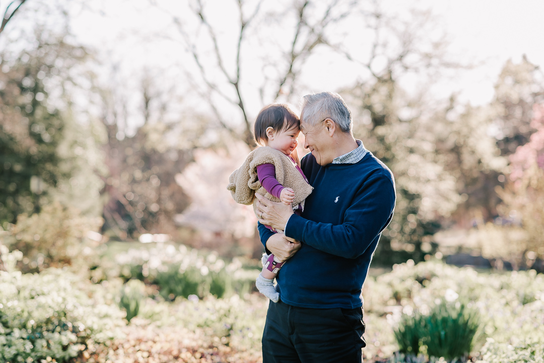 A happy grandfather touches foreheads with his toddler granddaughter sitting in his arms before visiting montessori schools in northern virginia