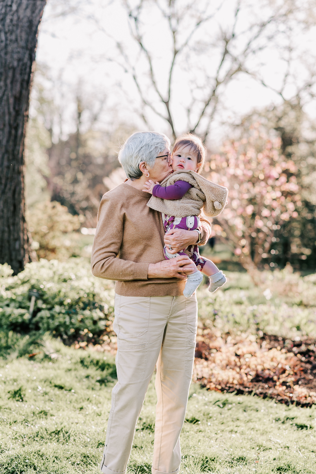 A grandmother stands in a yard kissing the cheek of heer toddler grandchild before visiting montessori schools in northern virginia