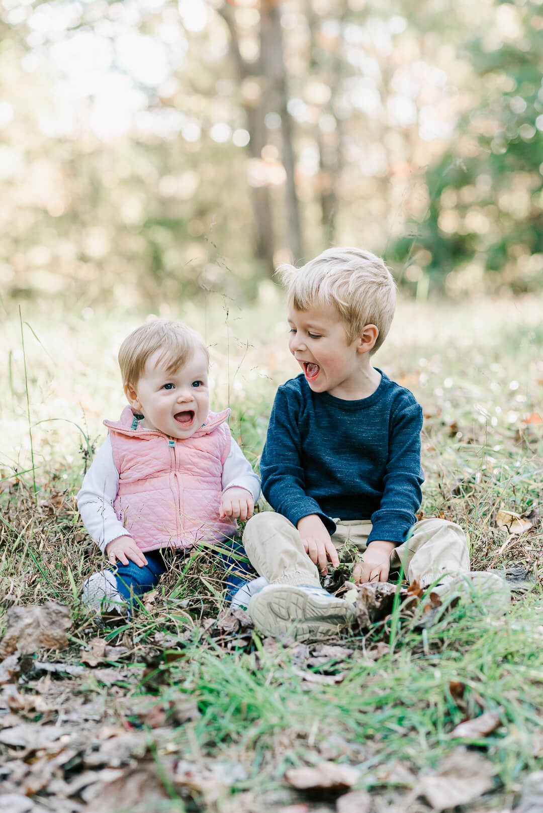 A happy toddler boy laughs and plays with his toddler baby sister in a park field