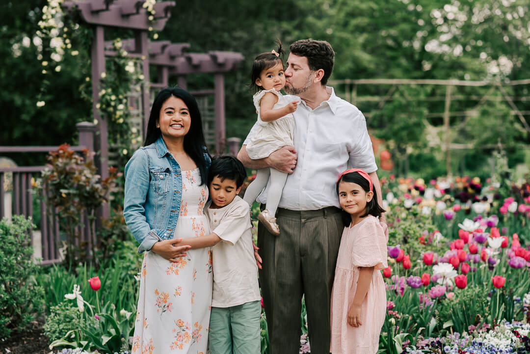 Happy parents stand in a colorful tulip garden with their toddler son and two toddler daughters before visiting kid friendly restaurants northern va