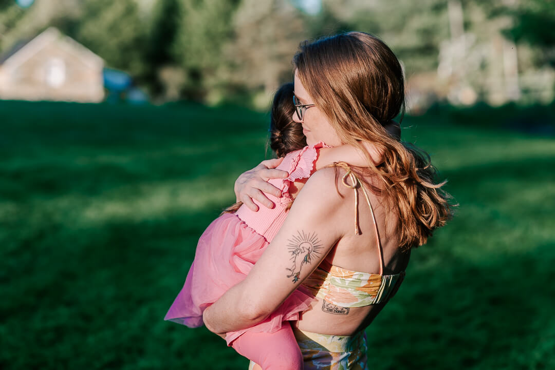 A mother hugs her toddler daughter tight while standing in a park lawn