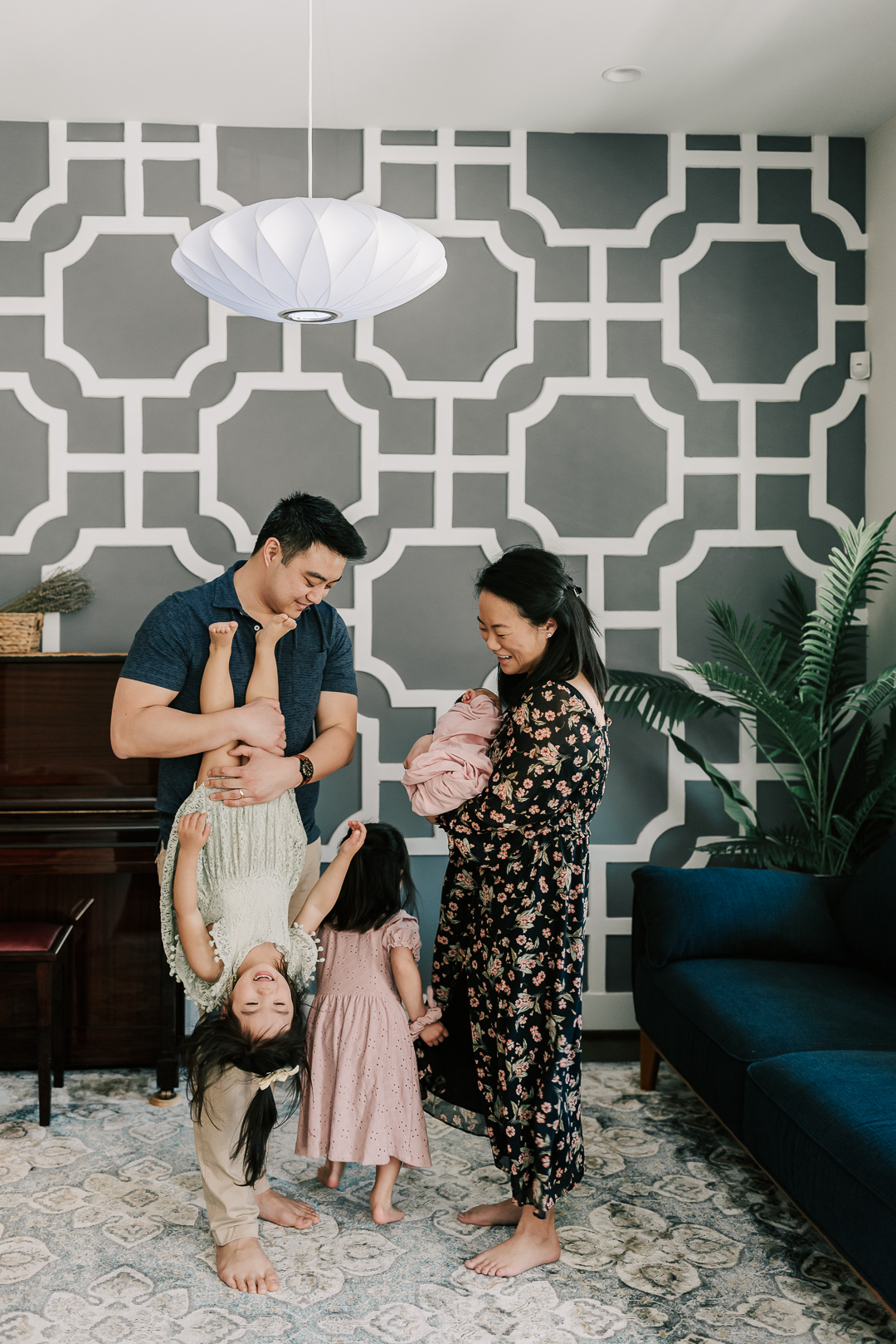 A mom and dad play and flip their toddler daughters while holding a newborn baby in a living room thanks to play therapy farifax pa