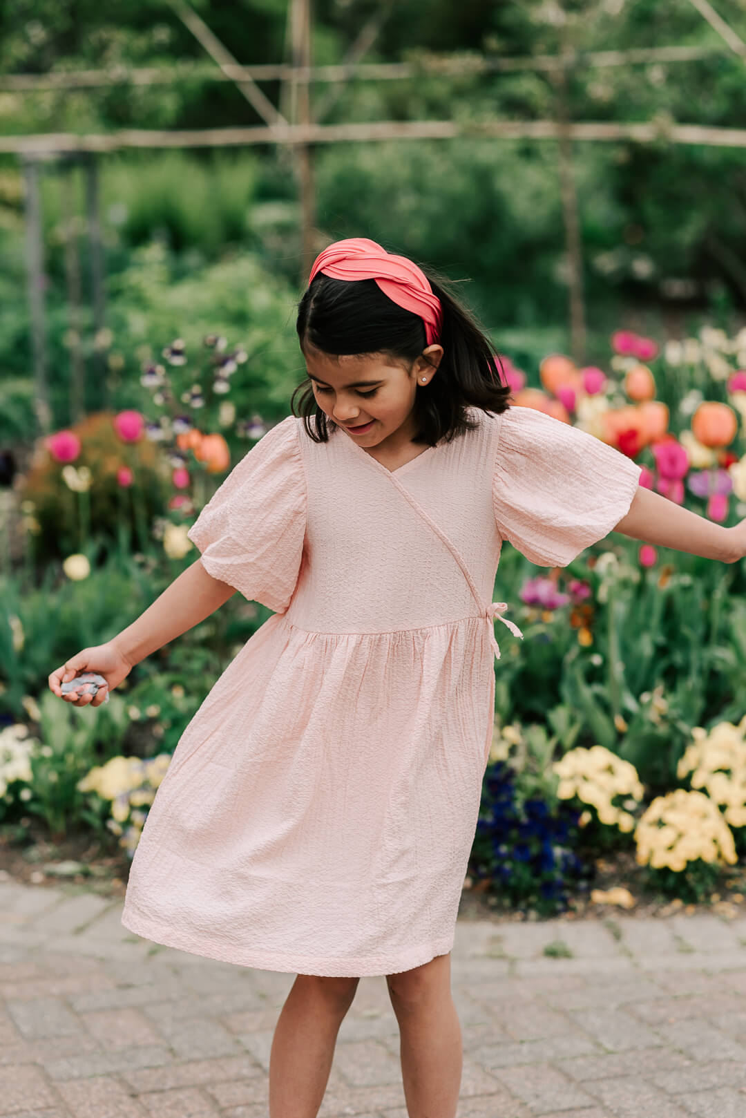 A young girl in a pink dress dances in a colorful garden path